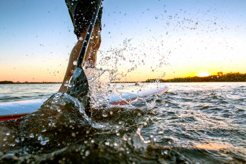 person on paddle board. Image is from knees down and you can see a large splash in the foreground from the paddle scooping water